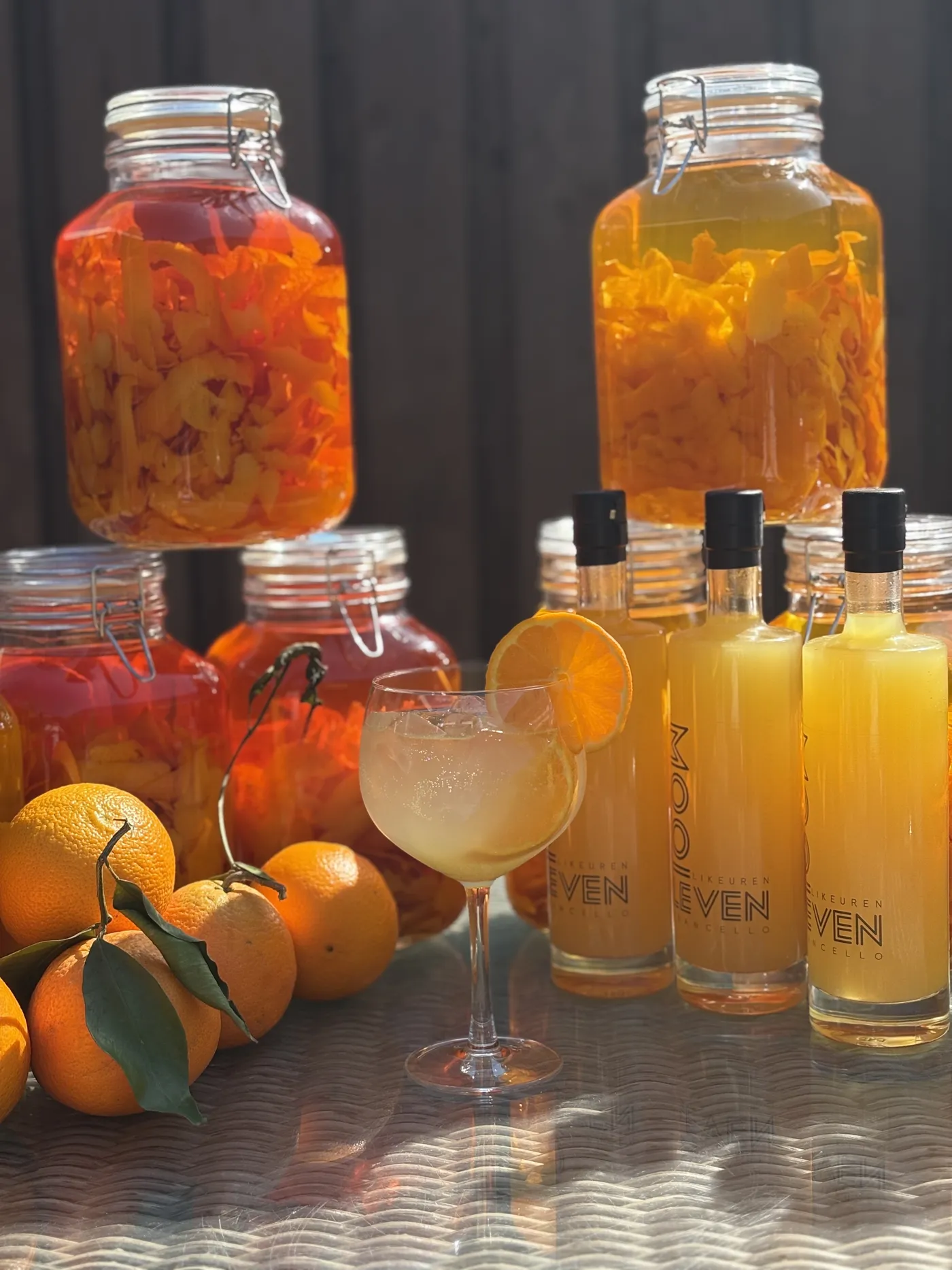 Grote weckpotten vol citroen- en sinaasappelschillen naast flessen likeur en een spritz